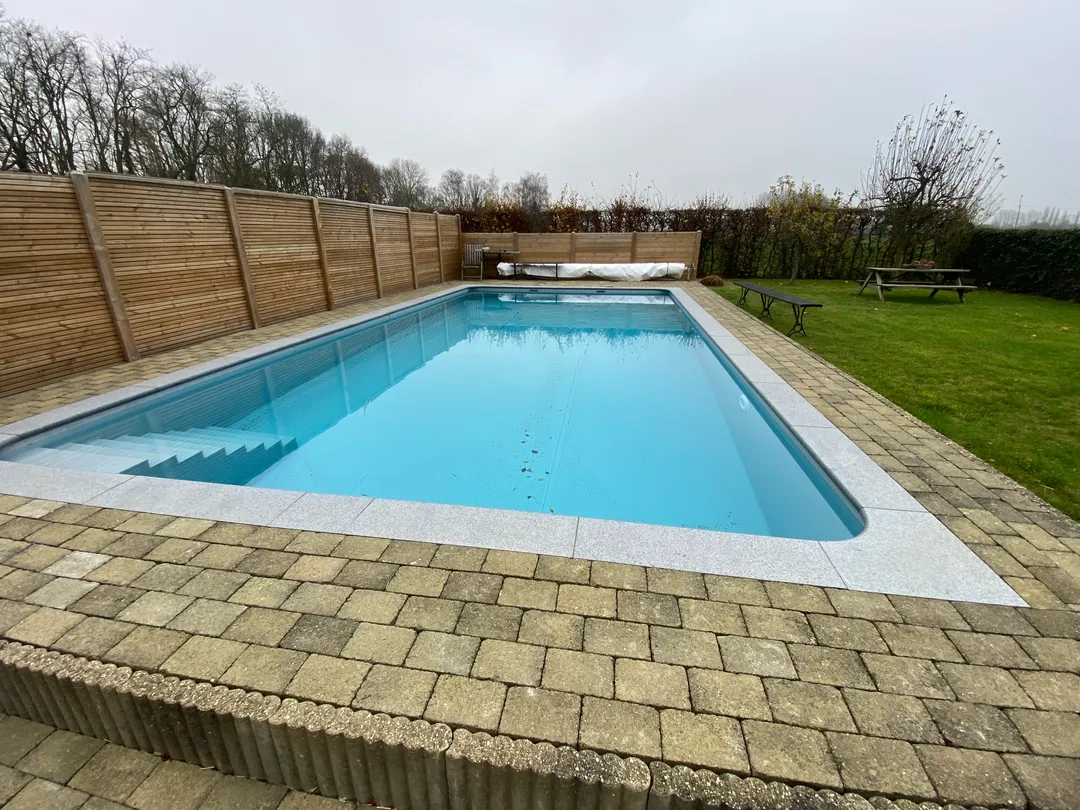 Gerenoveerd rechthoekig zwembad met nieuwe lichtblauwe zwembadliner en strakke grijze boordstenen