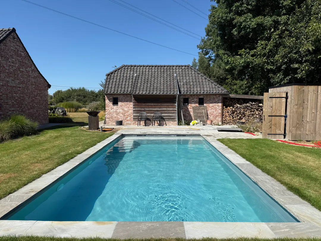 Gerenoveerd zwembad met strakke lichtblauwe zwembadliner en natuurstenen boord in een landelijke tuin