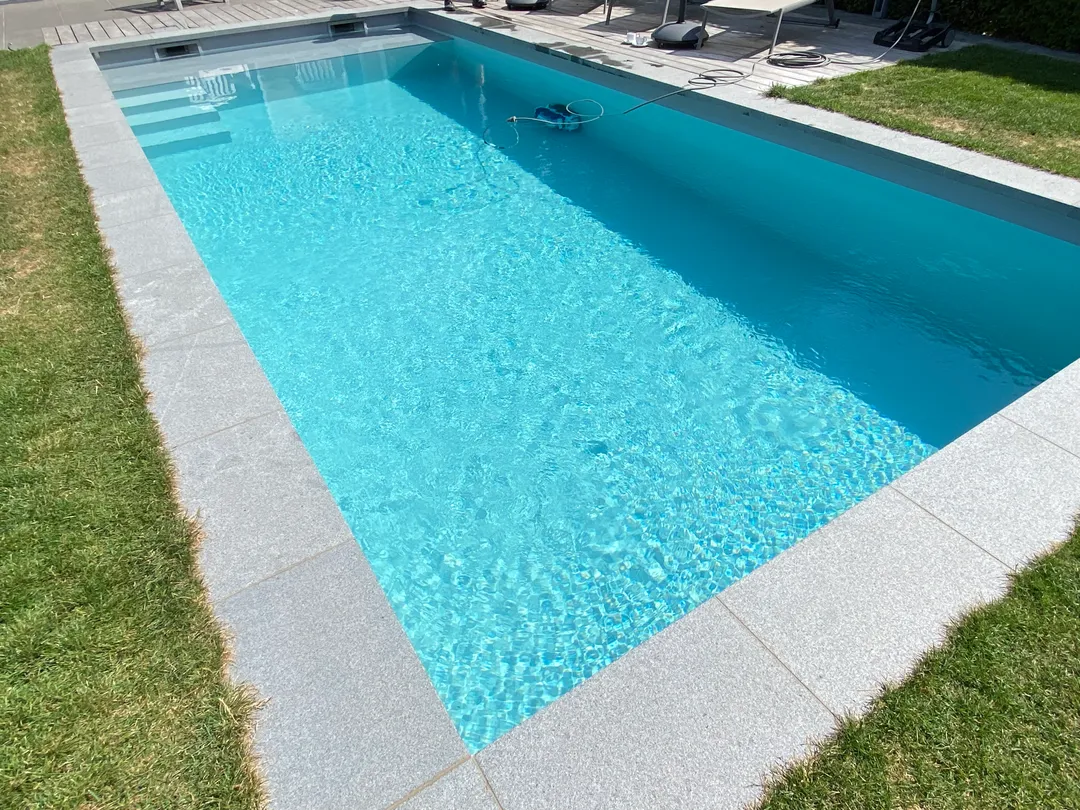 Strak afgewerkt zwembad met een nieuw geplaatste lichtblauwe liner en grijze boordstenen door Liner Plaatsen